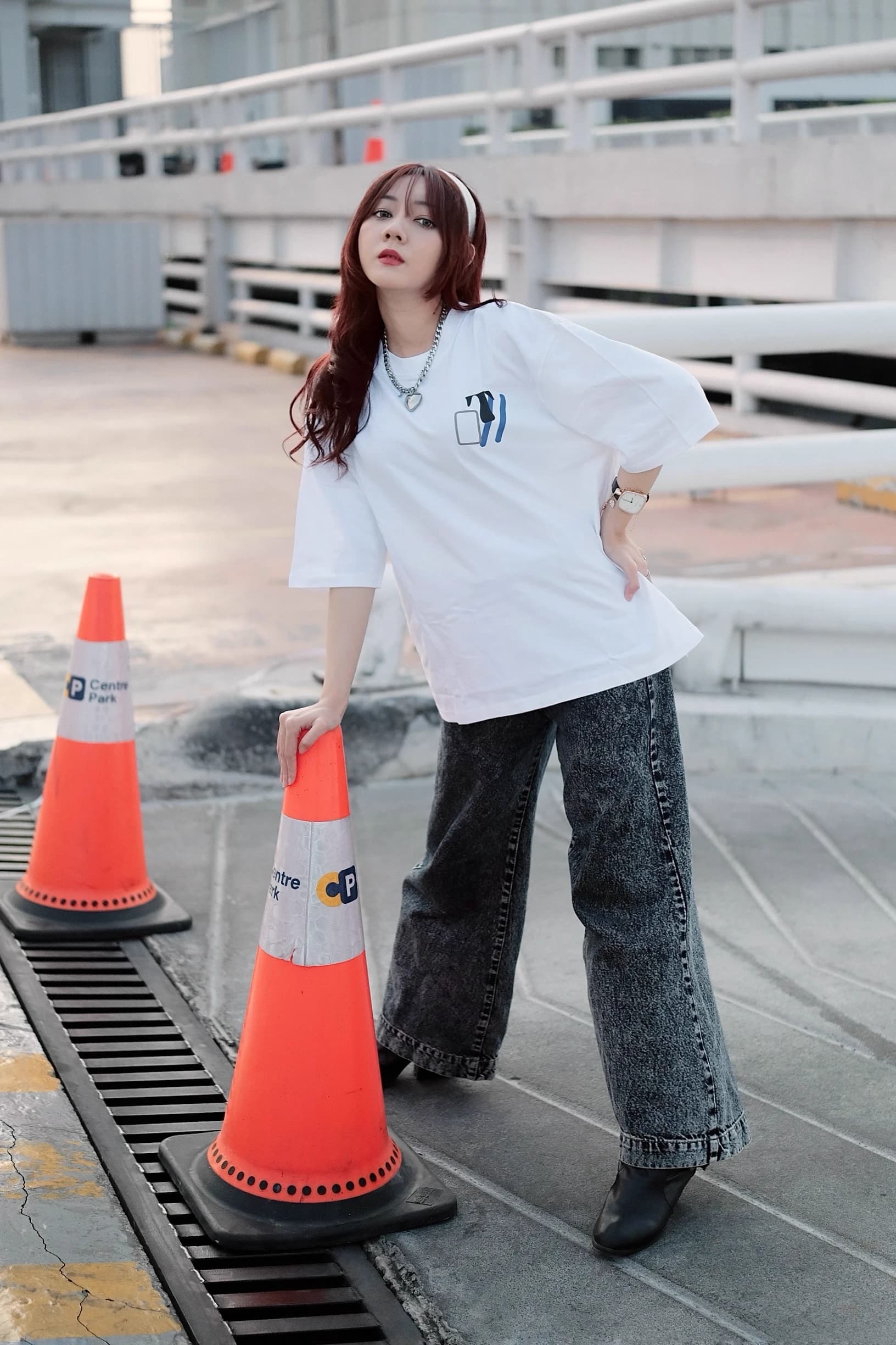 Woman in an oversized white graphic T-shirt posing beside traffic cones on a rooftop