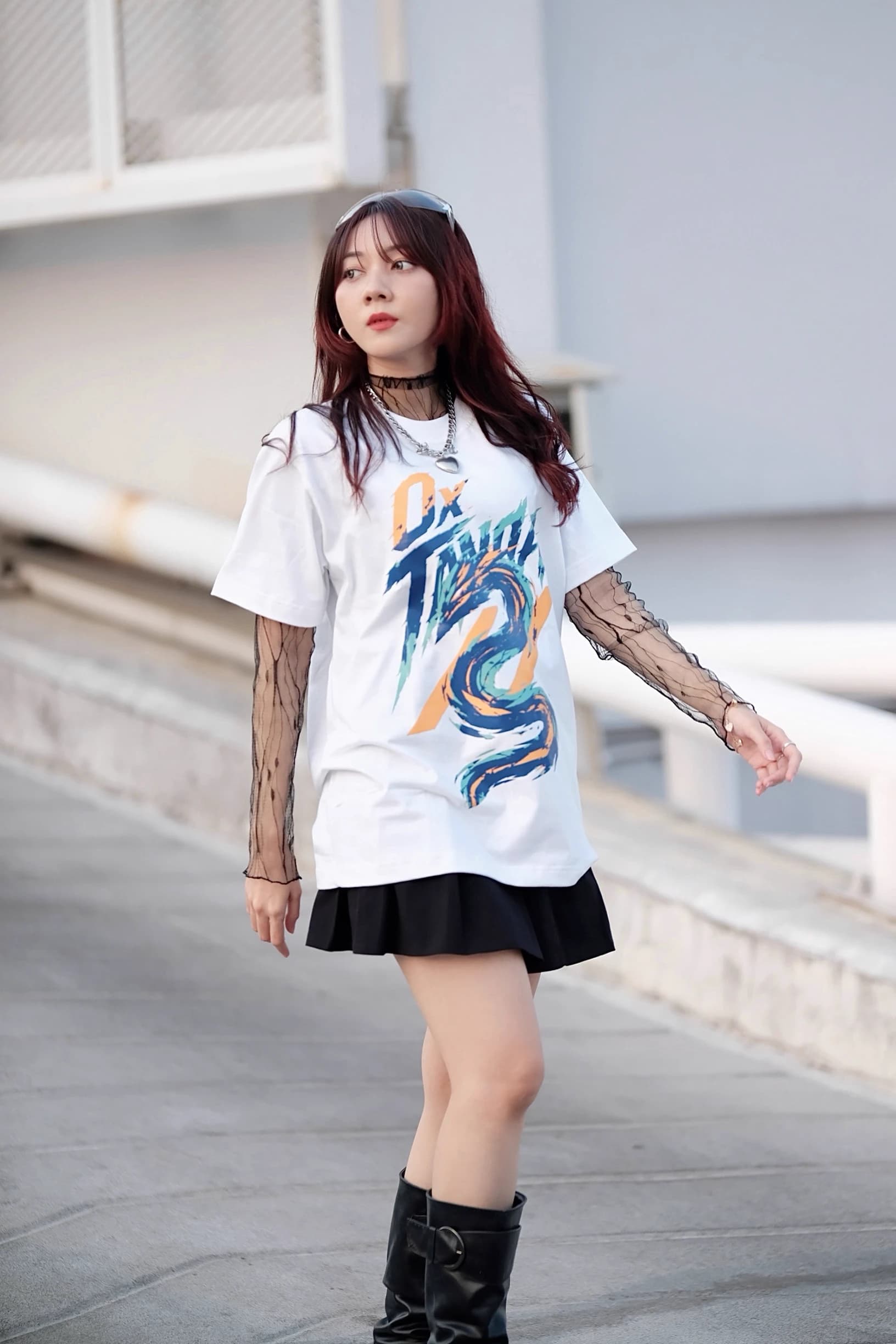 Woman walking on a rooftop in a white graphic T-shirt, black skirt, and boots