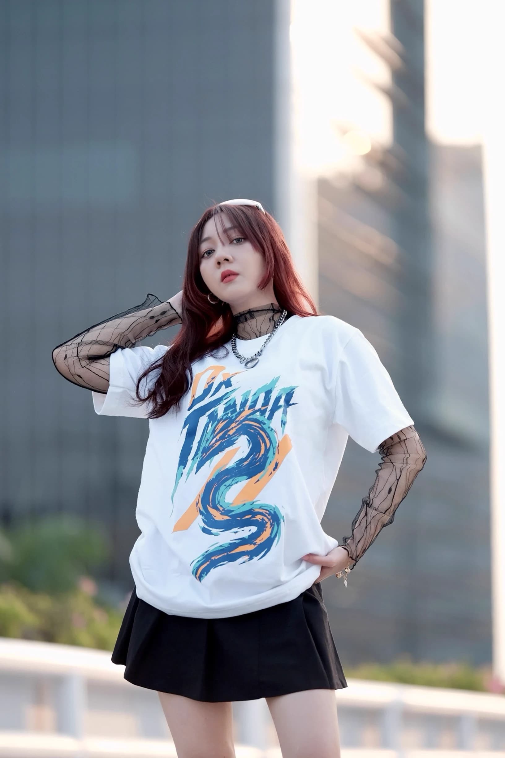 Woman posing on a rooftop in a white graphic T-shirt layered over sheer black sleeves